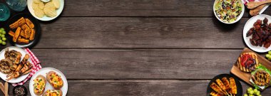 Yaz barbeküsü ya da piknik yemekleri çifte sınır. Hamburger, ızgara et, patates, mısır, meyve, salata ve aperatif. Koyu ahşap bir arkaplanda manzaranın üstünde. Boşluğu kopyala.