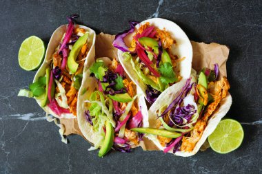 Avokado, lahana salatası ve kırmızı soğan turşulu tavuk sokak tacoları. Koyu taştan bir arkaplanda üst görünüm.