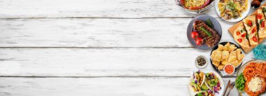 Çeşitli lezzetli yiyeceklerin yan sınırı. Beyaz ahşap bir arka planda tepeden aşağı manzara. Uzayı kopyala Makarna, ekmek, taco, biftek ve restoran temalı yemekler..