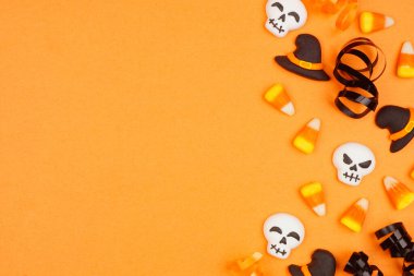 Cadılar bayramı kenarlarında siyah, beyaz ve turuncu renkli şeker ve kurdele var. Fotokopi alanı olan turuncu bir arkaplanda üstten aşağı görünüm.