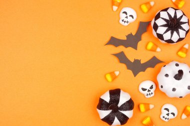 Cadılar Bayramı kenarlarında siyah, beyaz ve turuncu renkli şeker, yarasalar ve balkabağı dekoru. Fotokopi alanı olan turuncu arkaplan üzerindeki üst görünüm.