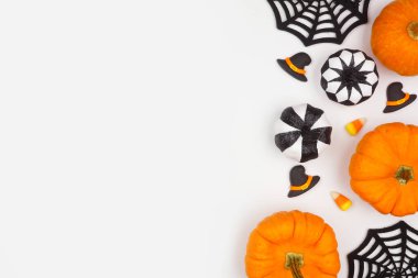 Cadılar Bayramı kenarlarında siyah, beyaz ve turuncu renkli şeker, balkabağı ve dekor var. Kopyalama alanı olan beyaz bir arkaplan üzerinde genel görünüm.