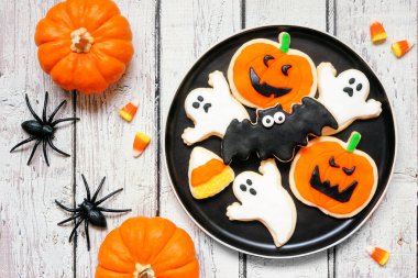 İçinde bir sürü ürkütücü Cadılar Bayramı kurabiyesi olan bir tabak. Beyaz ahşap masa zemininde dekor ile genel görünüm.