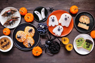 Karanlık ahşap arka planda ürkütücü Cadılar Bayramı kahvaltı masası sahnesi. Manzaranın üstünde. Krep, tost, yulaf ezmesi ve meyve çeşitleri..