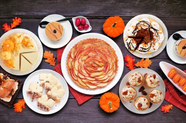 Sonbahar tatlıları, çeşitli gurmeler ve tatlı yiyecekler içeren bir masa sahnesi. Koyu bir ahşap arkaplan üzerinden yukarıdan aşağı görünüm.