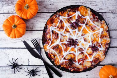 Cadılar Bayramı örümcek ağı pizzası. Kırsal beyaz ahşap arka planda tepedeki masa manzarası. Siyah kabuklu, yapışkan peynirli ve zeytinli örümcekler..