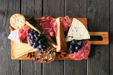 Peynir, et ve aperatiflerden oluşan şarküteri kurulu. Koyu bir ahşap arka planda tepeden aşağı manzara.