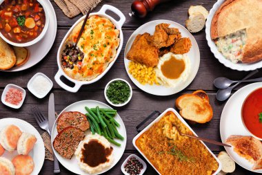 Konforlu yemek masası sahnesi. Koyu renk ahşap bir arka plan. Köfte, yahni, turta, fırında makarna, ızgara peynir, çorba, kızarmış tavuk, çoban böreği ve sıcak kenarlar..
