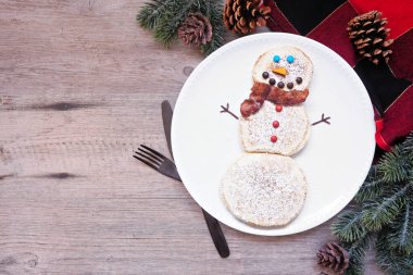Beyaz tabakta ahududu şapkalı ve muzlu sakallı şirin Noel Baba gözlemesi. Ahşap zemine karşı yukarıdan aşağı masa sahnesi.