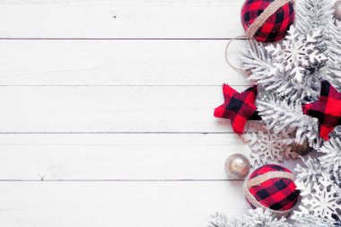 Kırmızı ve siyah gingham süslerinden, karlı dallardan ve altın takılardan oluşan bir Noel kenarı. Beyaz ahşap arka planda yukarıdan görüntü. Boşluğu kopyala.