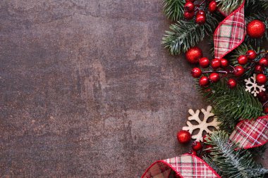 Kırmızı ekose kurdeleler, takılar, kar taneleri ve soğuk dallardan oluşan bir Noel kenarı. Koyu kahverengi arka planda üst manzara. Boşluğu kopyala.