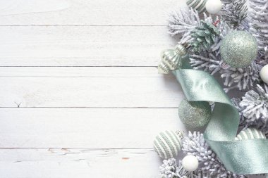 Yumuşak yeşil süsler, kurdele ve karlı ağaç dallarından oluşan bir Noel kenarı. Beyaz ahşap arka planda tepeden aşağı manzara. Boşluğu kopyala.