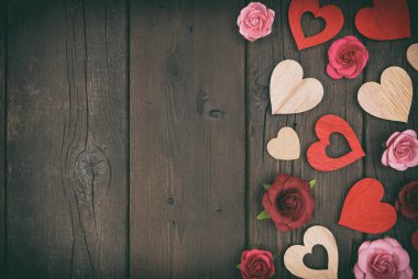 Sevgililer Günü 'nde tahta kalpler ve kağıt güllerden oluşan bir sınır. Koyu renk ahşap arka planda üst manzara. Bağbozumu etkisi. Boşluğu kopyala.