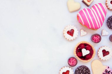 Sevgililer Günü 'nde çeşitli kurabiyeler, çikolatalar ve şekerlerle yan sınırda yemek pişirmek. Fotokopi alanı olan beyaz mermer bir arka plan. Aşk ve kalp teması.