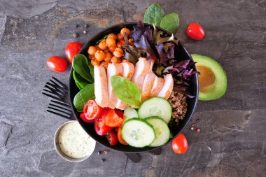 Healthy homemade salad bowl with avocado, chickpeas, quinoa and vegetables. Top view with frame of ingredients on a dark slate background. clipart