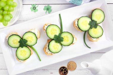 Aziz Patrick Günü yoncalı çay sandviçlerini krem peynir ve salatalıkla açıyorum. Beyaz ahşap bir arkaplan üzerinde üst görünüm tablo sahnesi.