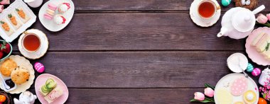 Paskalya ya da ilkbahar çayı koyu renkli ahşap bir arka planda çifte sınır oluşturur. Çeşitli parmak sandviçler, çörekler ve tatlı tatlılar. Üst Manzara. Boşluğu kopyala.