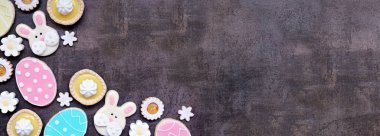 Paskalya ya da bahar temalı fırın köşesi kenarlarında çeşitli kurabiyeler ve tatlı tatlılar. Fotokopi alanı olan koyu taştan bir arkaplan üzerindeki en üst görünüm.