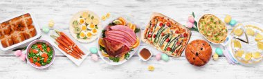 Geleneksel Paskalya jambonu yemeği. Masanın üstünde beyaz ahşap bir afiş var. Jambon, istiridyeli patates, sebze tabağı, yumurta, ekmek ve limonlu tatlı..
