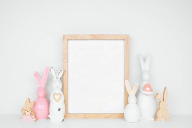 Modern Paskalya ev dekorasyonu sahnesi. Beyaz bir rafta paskalya tavşanlarıyla portre ahşap çerçeve yap. Boşluğu kopyala.