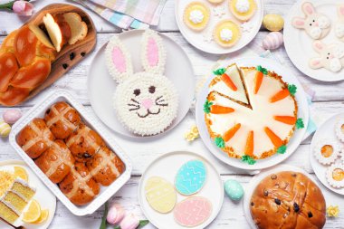 Paskalya ya da bahar tatlı masası sahnesi. Beyaz ahşap arka planda yukarıdan aşağıya doğru. Tavşan keki, renkli kurabiyeler, ekmekler, turtalar ve çeşitli tatlılar..