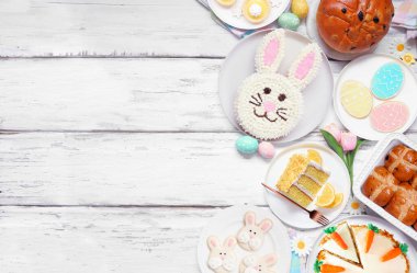 Paskalya ya da bahar tatlısı sınırında. Beyaz ahşap bir arka plan üzerinden yukarıdan görünüyor. Tavşan keki, renkli kurabiyeler, ekmekler, turtalar ve çeşitli tatlılar. Boşluğu kopyala.