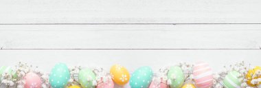 Pastel Paskalya yumurtaları ve beyaz bahar çiçekleri. Beyaz ahşap bir arkaplan ile alt sınırın yukarıdan görünüşü. Boşluğu kopyala.
