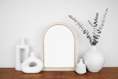 Modern vazo dekoruyla ahşap kemerli portre çerçevesi yap. Beyaz bir duvara karşı ahşap bir raf. Boşluğu kopyala.