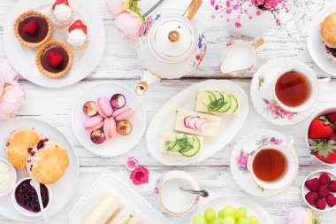 Akşamüstü çay masası sahnesi beyaz ahşap arka planda. Klasik çay seti, parmak sandviçler, çörekler ve tatlılar. Genel Görünüm.