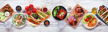 Sağlıklı bitki temelli vejetaryen yemek masası sahnesi. Beyaz ahşap bir arka planda yukarıdan görüntü. Jackfruit burger, mantarlı taco, karpuz ve karnabahar bifteği, havuç sosisi, cevizli bolonez