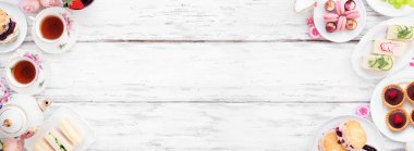 Akşamüstü çayı beyaz ahşap bir arka planda çifte sınır oluşturur. Klasik çay seti, parmak sandviçler, çörekler ve tatlılar. Kopyalama alanı ile görünümün üstünde.