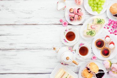 Akşamüstü çay kenarı sınırına karşı beyaz bir tahta arka plan. Klasik çay seti, parmak sandviçler, çörekler ve tatlılar. Kopyalama alanı ile genel görünüm.