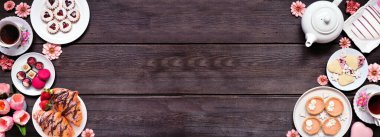 Anneler Günü çayı koyu ahşap bir arka planda çifte sınır oluşturur. Tatlı tatlılar ve hamur işleri seçimi. Manzaranın üstünde. Pembe çiçek ve kalp teması.