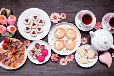 Anneler Günü çay masası sahnesi koyu ahşap arka planda. Tatlı tatlılar ve hamur işleri çeşitleri. Üst Manzara. Pembe çiçek ve kalp teması.