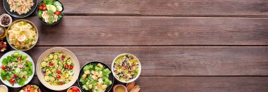 Lezzetli ev yapımı salata çeşitleri. Koyu renk ahşap bir arka planda tepenin köşesi. Yaz yemekleri konsepti. Patates, sezar, makarna ve yeşil salata..