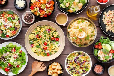 Lezzetli ev yapımı salata çeşitleri. Koyu renk ahşap arka planda en üstteki masa sahnesi. Yaz yemekleri konsepti. Patates, sezar, makarna ve yeşil salata..