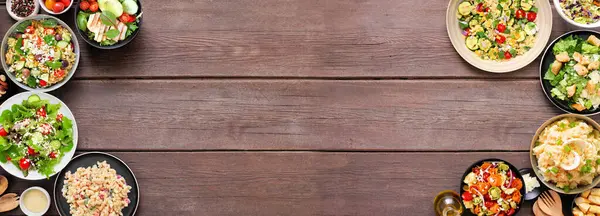 Lezzetli ev yapımı salata çeşitleri. Koyu ahşap bir arka planda üst manzara çift kenar. Yaz yemekleri konsepti. Patates, sezar, makarna ve yeşil salata..
