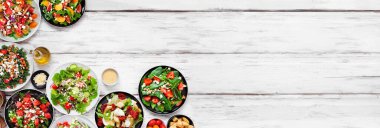 Lezzetli taze salataların çeşitleri. Beyaz ahşap bir arka planda, köşedeki sınırın üstünde. Yaz yemekleri konsepti.