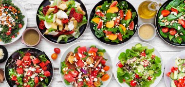 Lezzetli taze salata çeşitleri. Beyaz ahşap bir arka planda yukarıdan görünen masa sahnesi. Yaz yemekleri konsepti.