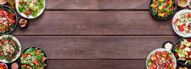 Lezzetli taze salataların çeşitleri. Koyu renk ahşap bir arka planda çift kenar manzaralı. Yaz yemekleri konsepti.