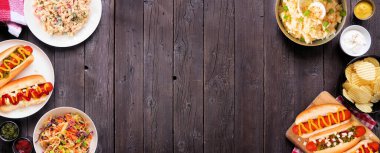 Sosisli sandviçler, klasik salatalar ve abur cuburlarla barbekü. Masa manzarasının üstünde koyu ahşap bir afiş var. Boşluğu kopyala.