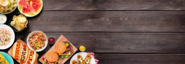 Sosisli, hamburgerli ve kenarlı yaz yemekleri sahnesi. Karanlık ahşap bir arka planda, köşedeki sınırın üstünde. Boşluğu kopyala.