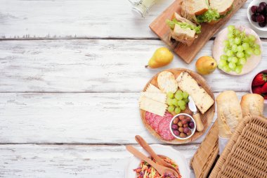 Yaz pikniği yan sınırı. Beyaz ahşap arka planda üst manzara. Piknik sepeti, meyve, salata, sandviç ve atıştırmalıklar. Boşluğu kopyala.