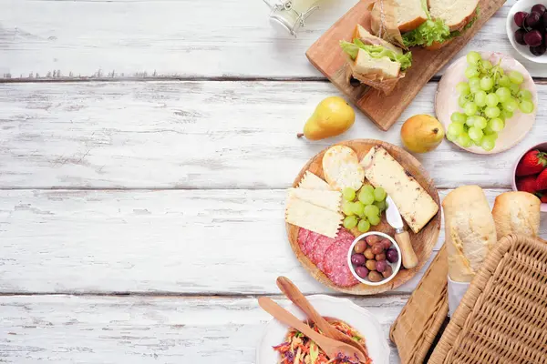 Yaz pikniği yan sınırı. Beyaz ahşap arka planda üst manzara. Piknik sepeti, meyve, salata, sandviç ve atıştırmalıklar. Boşluğu kopyala.
