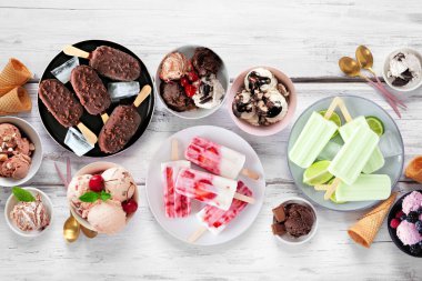 Harika bir yaz yemeği masası sahnesi. Çeşitli dondurma kaseleri, buzlu dondurmalar ve dondurulmuş ikramlar. Beyaz ahşap zemin üzerinde görünüm.