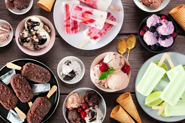 Harika bir yaz yemeği masası sahnesi. Dondurma kaseleri, buzlu dondurmalar ve dondurulmuş ikramlar. Koyu bir ahşap arka planda manzaranın üstünde.