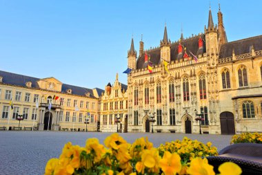 Bruges Belediye Binası. Sıcak gün batımının altında. Önünde sarı çiçekler, Belçika.