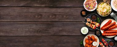 Koyu renk ahşap bir arka plan üzerinde yaz barbekü yemek kenarı sınırı. Çeşitli ızgara etler, salatalar ve kenarlar. Üst görünüm.