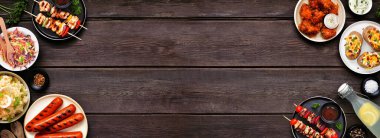 Summer BBQ food double border over a dark wood banner background. Variety of grilled meats, salads and sides. Above view.