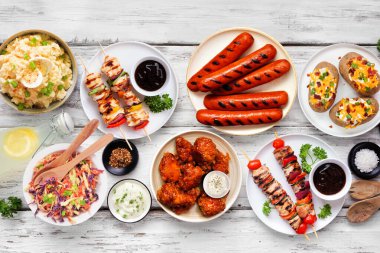 Beyaz ahşap arka planda yaz barbekü masası sahnesi. Çeşitli ızgara etler, salatalar ve kenarlar. Üst alt görünüm.